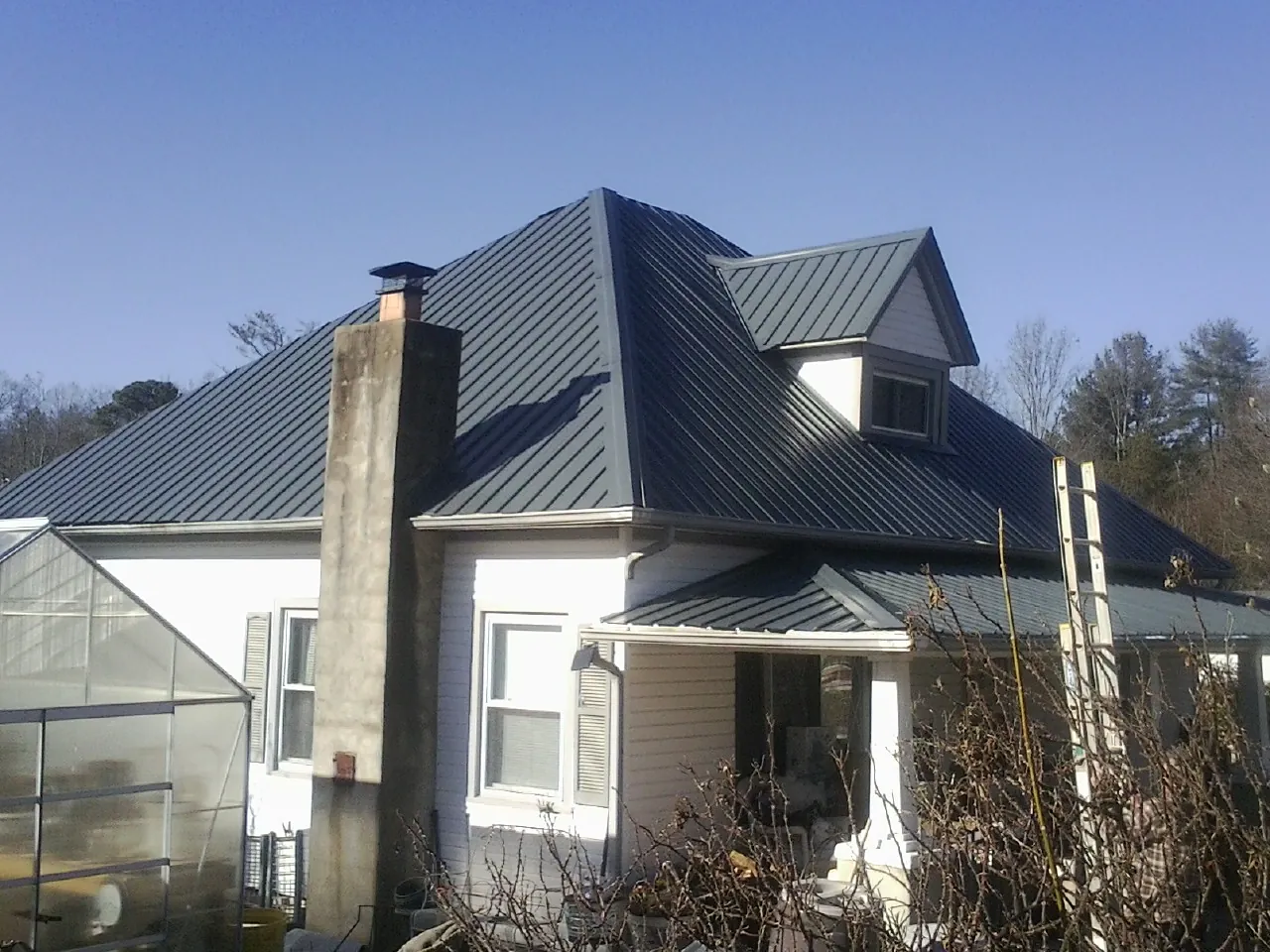 Dark blue standing seam metal roof on a white farmhouse with dormer — Slate & Tile Roof Repair by Roofing Brothers in Higginsville