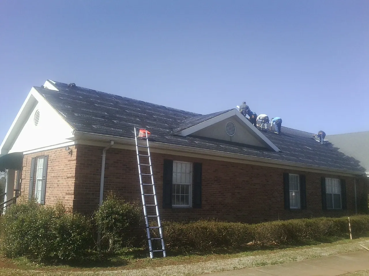 Crew tearing shingles off a brick ranch roof with a ladder set — Emergency Roof Repair work by our crew in Higginsville