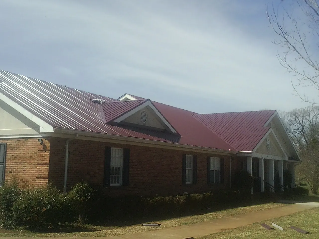 Red metal roof with gabled entries on a long brick building, from a Hail Damage Roof Repair job in Higginsville
