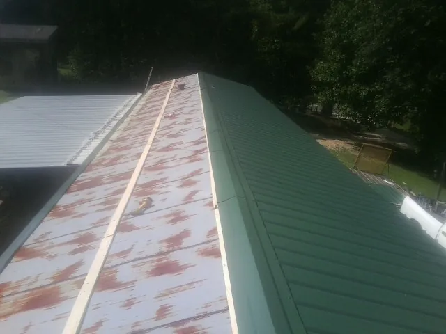 Old rusted panels beside newly installed green metal roofing — Wind Damage Roof Repair by Roofing Brothers in Higginsville