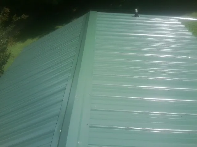 New green metal panels meeting at the ridge of a roof — Flat Roof Repair work by our crew in Higginsville