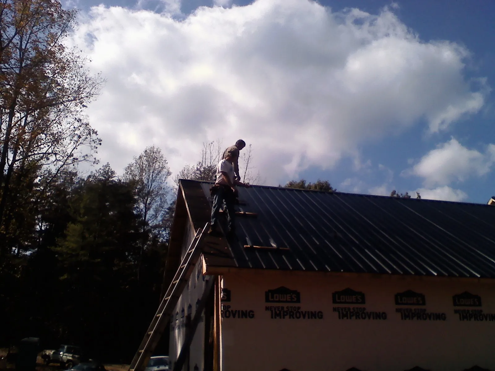 Roofer fastening dark metal panels high against a cloudy sky, from a Roof Inspection job in Higginsville