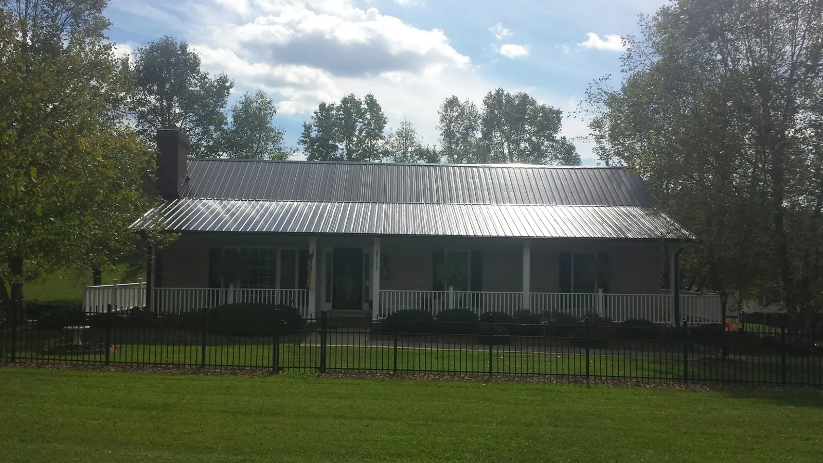 Gray metal roof on a brick ranch with a full width front porch — Gutter Guard Installation work by our crew in Higginsville