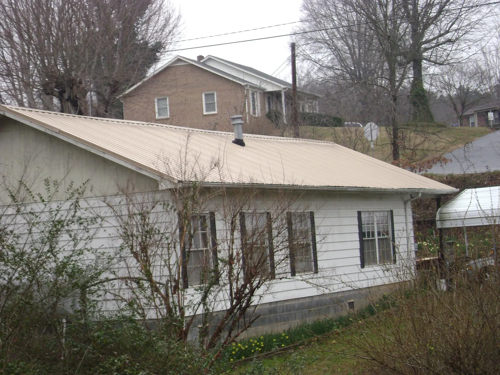 Tan metal roof on a white sided house set into a hillside — Commercial Roofing by Roofing Brothers in Higginsville