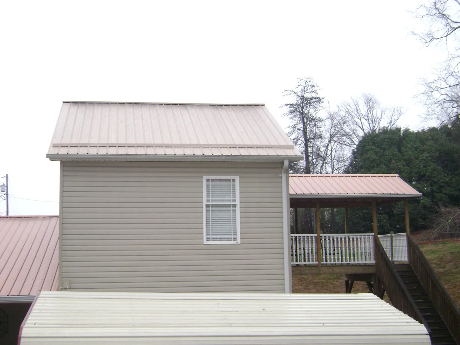 Tan metal roofs on a two story addition and attached porch, from a Roof Replacement job in Higginsville